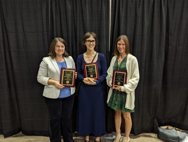 Rising Scholars Erin Nelson, Sarah Baires, and  Melissa Baltus hold their award plaques excitedly. 